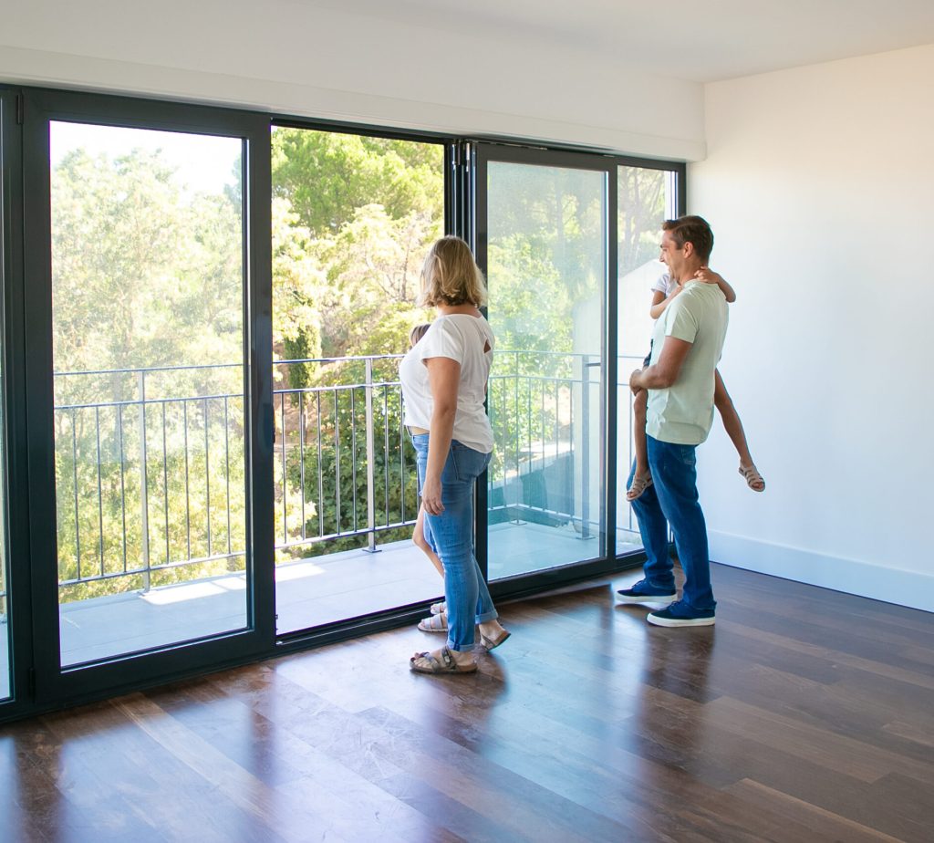 Happy family with kids looking at balcony and smiling. Back view of blonde mother. Daughter sitting on father hands. People watching new house or flat. Mortgage, relocation and moving day concept